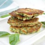 stack of spinach & feta savory pancakes on a white platter surrounded by spinach leaves