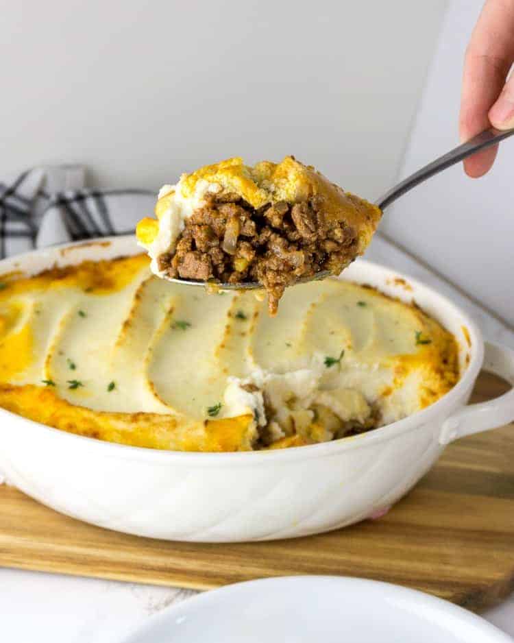 hand holding spoon lifting serving of keto Shepherd's pie onto white plate