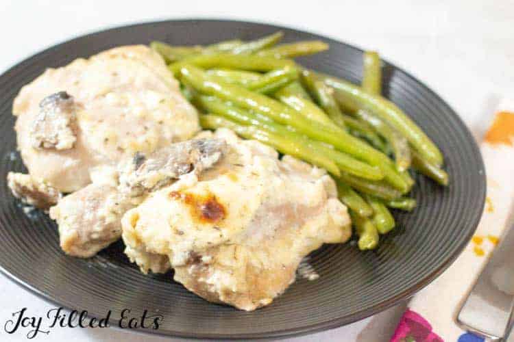 Baked chicken thighs with mushrooms served on a black plate with a side of green beans