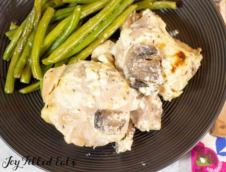 Baked chicken thighs with mushrooms served on a black plate with a side of green beans from above