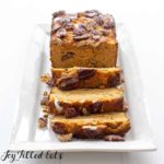 pumpkin bread loaf topped with pecans on a white platter with three slices cut from loaf