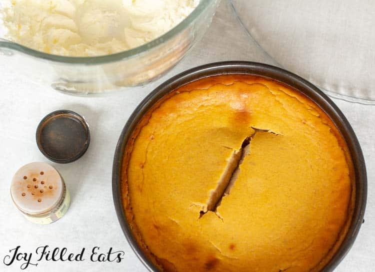 low carb pumpkin cheesecake in springform pan next to bowl of whipped cheesecake topping