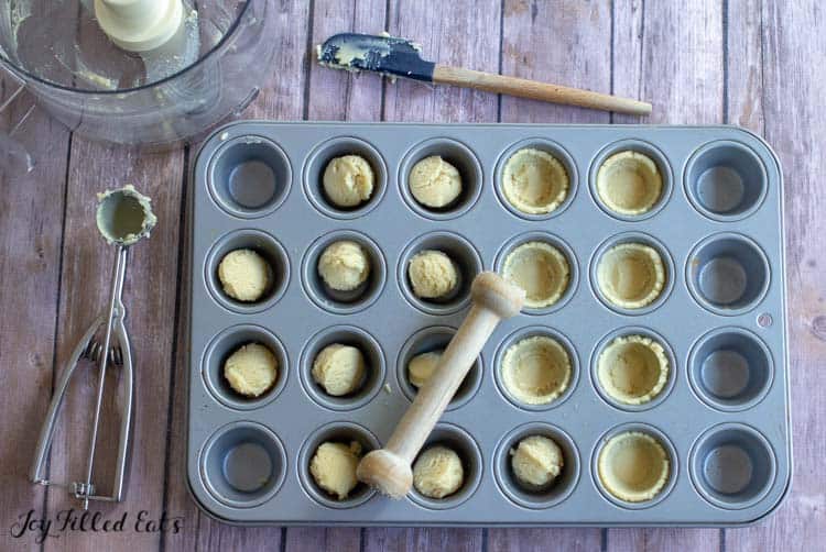 mini muffin tin filled with pie crusts with half being shaped into small pie crusts by wooden dowel