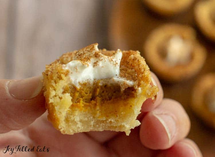 hand holding a mini pumpkin pie with a large bite missing