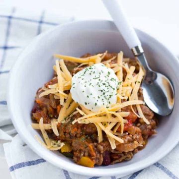 spoon and bowl of slow cooker no bean chili topped with sour cream and shredded cheese