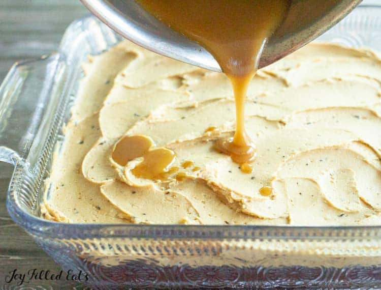 caramel sauce being poured onto iced brownies in baking dish