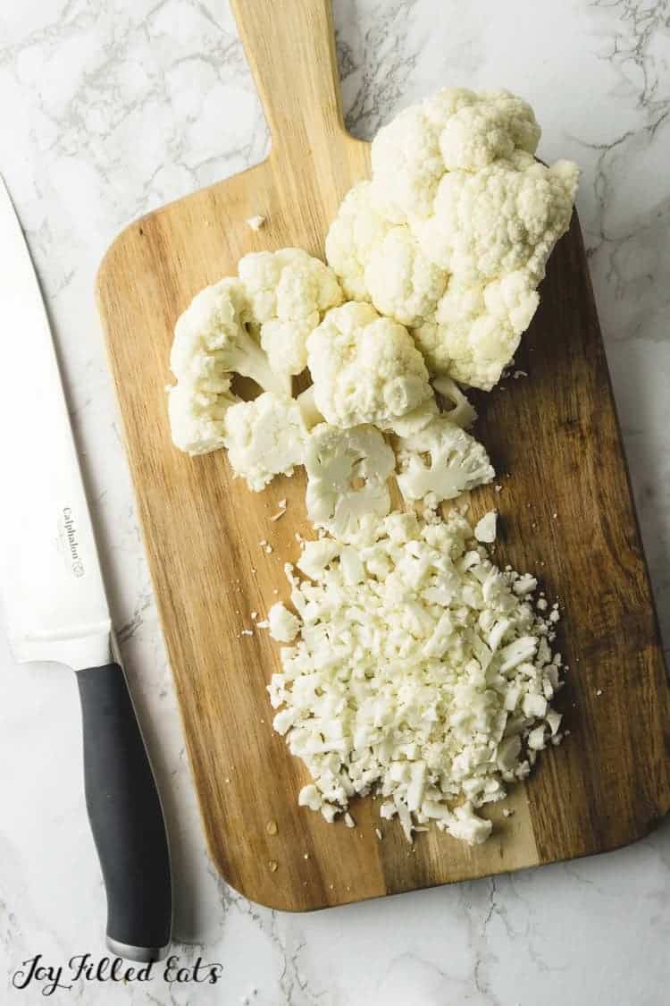 cutting board of cauliflower head portions and finely chopped cauliflower next to chef's knife