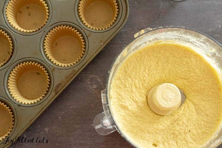 batter in food processor next to wrapper lined muffin tin