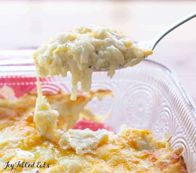 spoonful of hashbrown casserole being lifted from casserole dish below