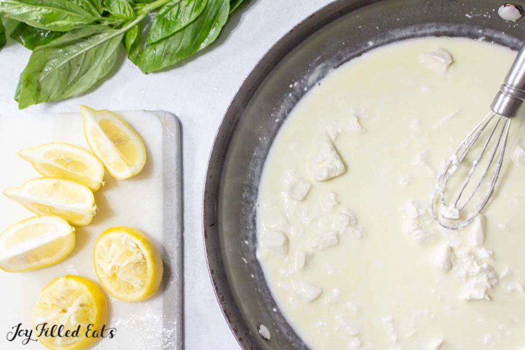 overhead view of cream sauce in skillet with whisk next to a cutting board of lemon wedges