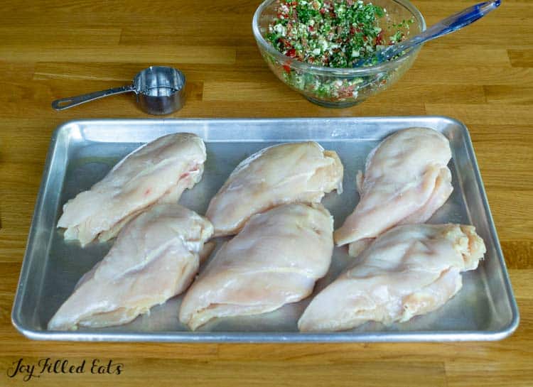 Chicken breasts on a sheet pan next to a bowl of Greek Salad filling
