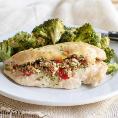 Baked Chicken Breast stuffed with Greek Salad served with a side of broccoli florets on a white plate