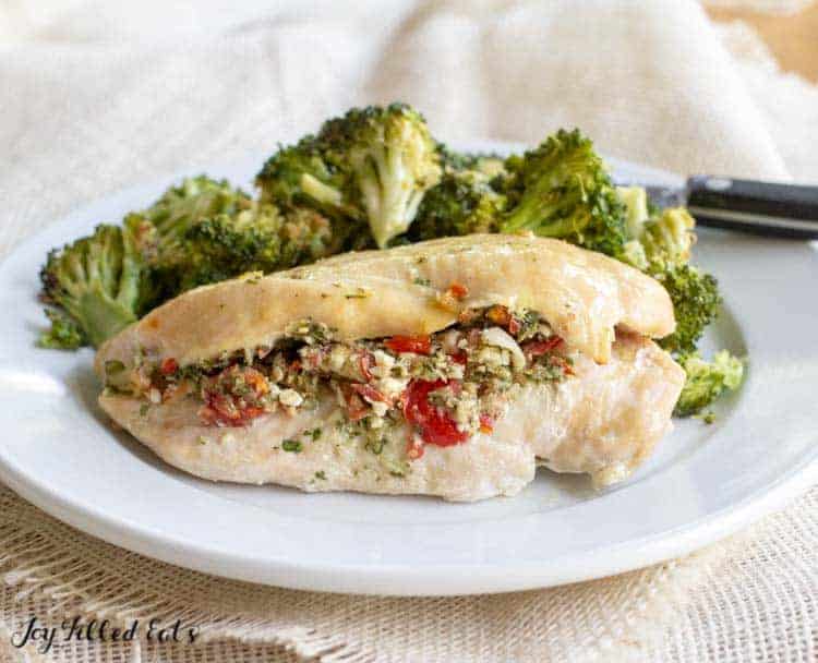 Baked Chicken Breast stuffed with Greek Salad served with a side of broccoli florets on a white plate