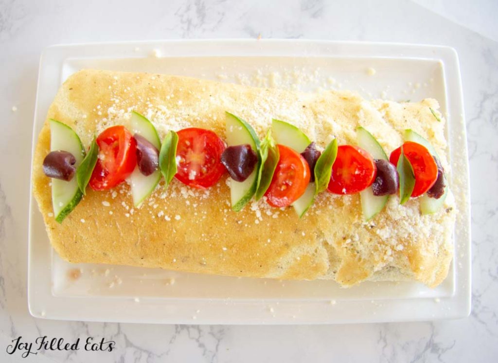 overhead view if greek salad roulade topped with cucumber slices, tomato slices and olive slices