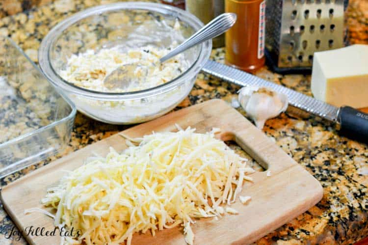 cutting board of shredded cheese next to mixing bowl of dip ingredients with spoon