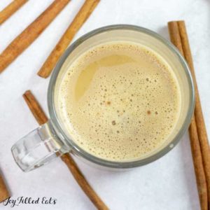 overhead view of Snickerdoodle latte in a glass mug surrounded by cinnamon sticks