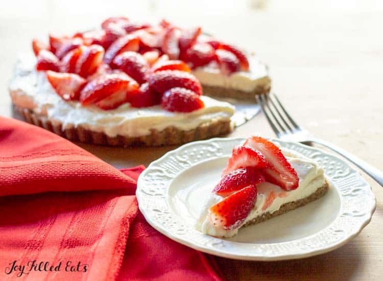 slice of strawberry tart on a white plate set next to remaining strawberry tart in a pie tin and fork