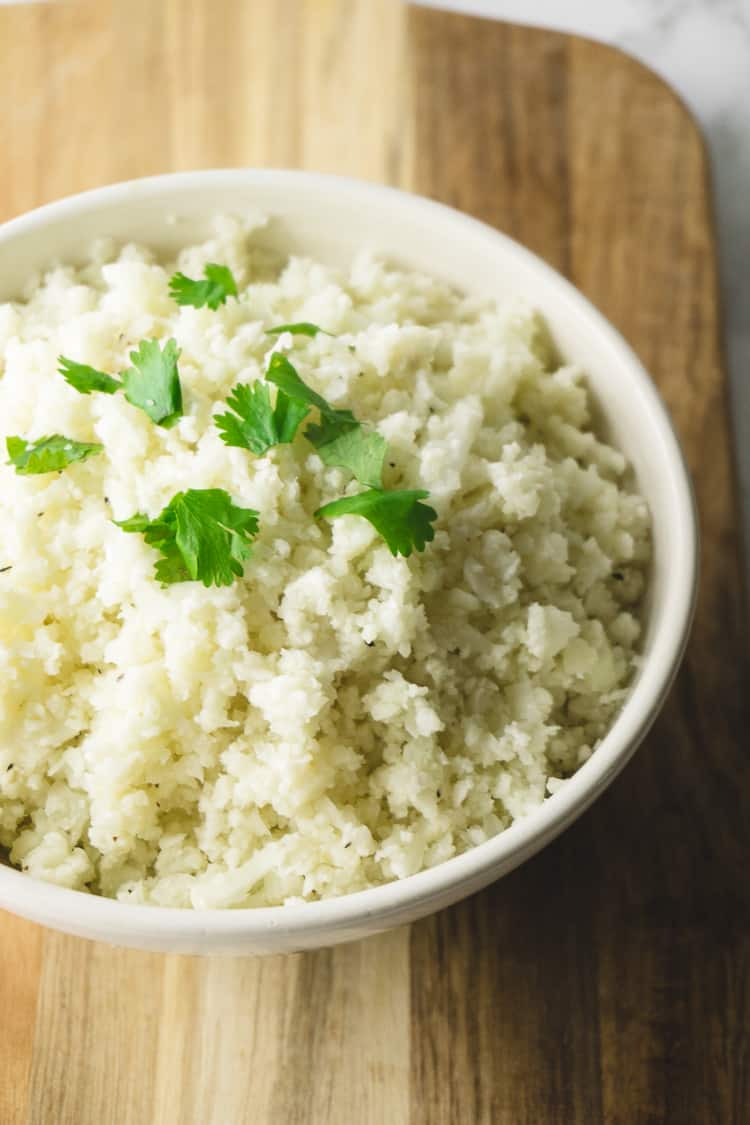close up on bowl of riced cauliflower topped with fresh herbs