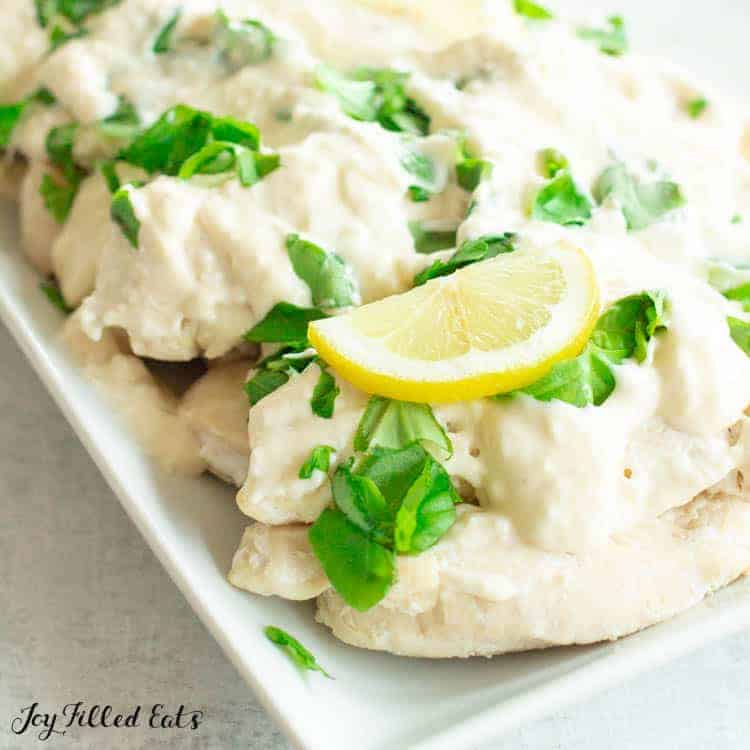 Close up of chicken topped with chopped basil and a slice of lemon