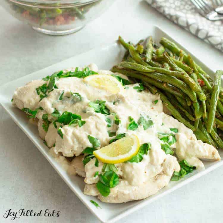 Platter of Creamy Lemon Chicken topped with chopped basil and a slice of lemon served next to green beans