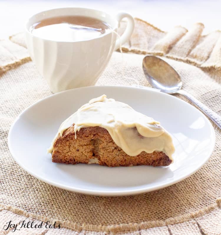 maple oat nut scones with a glaze icing on a plate next to a spoon and cup of coffee