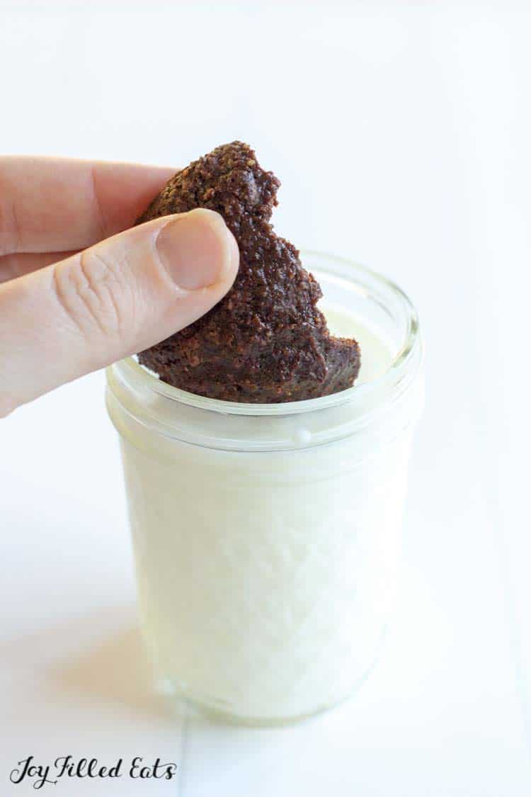 hand dunking half a brownie cookie into a mason jar of milk