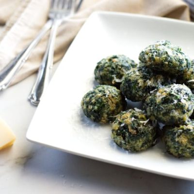 pile of spinach balls topped with Parmesan set on a table with forks, Parmesan rind and grater