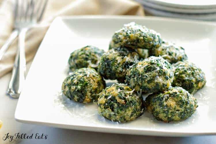 pile of spinach balls topped with parmesan on a square white plate on a table with forks