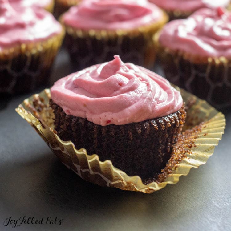 close up on a chocolate champagne cupcake with raspberry icing with the wrapper slightly removed