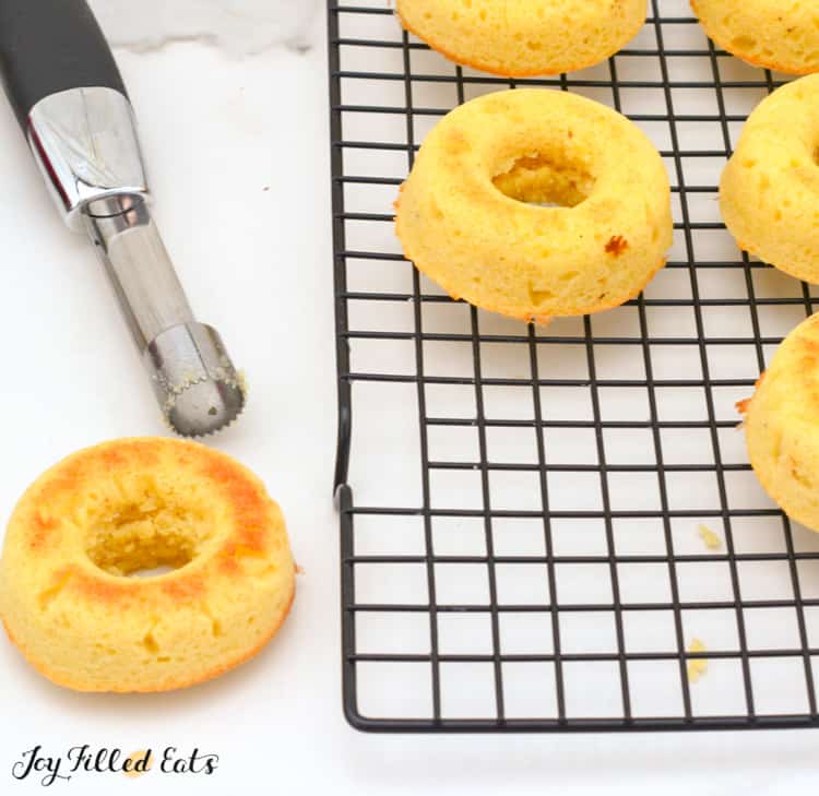 vanilla donuts on a cooling rack next to corer utensil