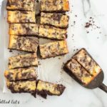 rows of cheesecake brownie bars with two bars sitting on a spatula