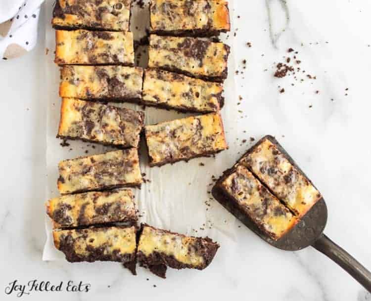 rows of cheesecake brownie bars with two bars sitting on a spatula