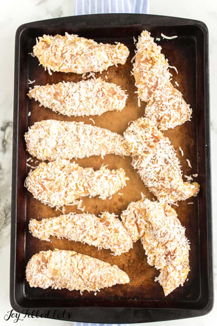 sheet pan lined with coconut chicken tenders before baking
