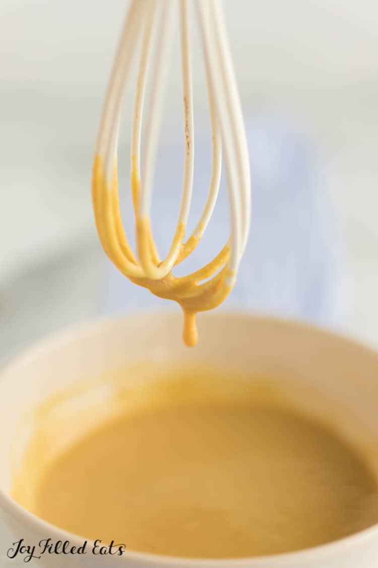 whisk dripping in maple mustard sauce from bowl below