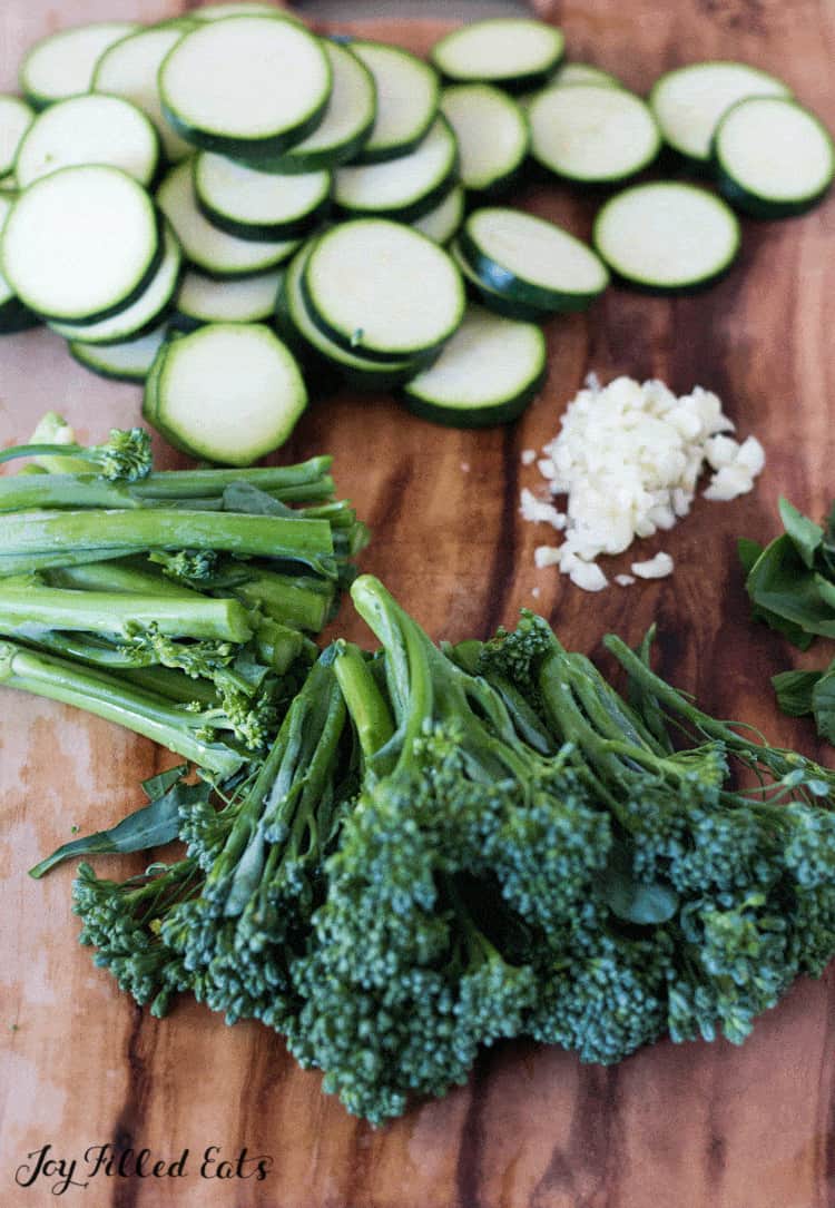 sliced cucumbers, minced garilc and chopped broccolini on a cutting board