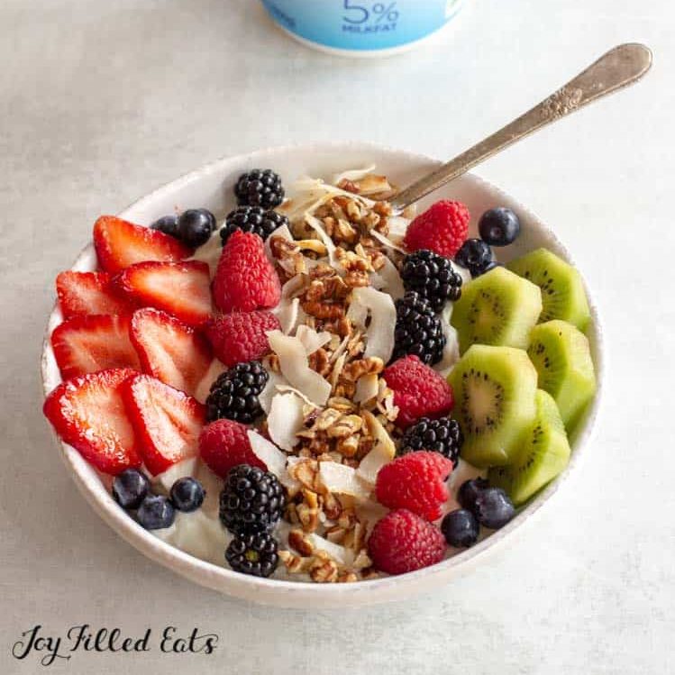 large bowl of yogurt with fruit and keto granola set in front of a container of Fage Total yogurt