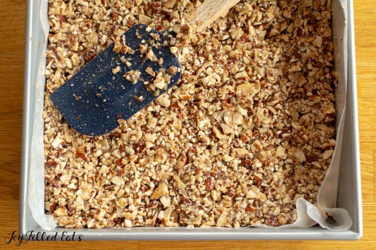 spatula spreading granola mixture into bottom of baking dish