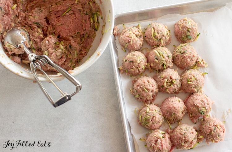 large bowl and ice cream scoop of turkey meatball mixture next to a sheet pan lined with turkey meatballs