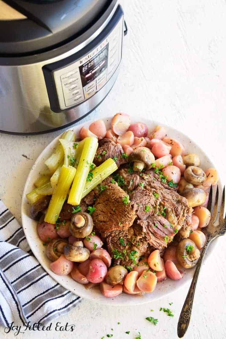 platter of pot roast surrounded by vegetables set in front of an instant pot