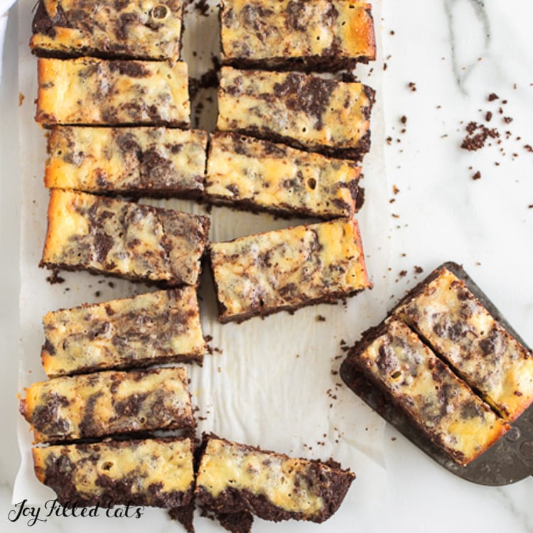 overhead view of keto cheesecake brownies cut into bars on parchment paper. two bars placed on spatula