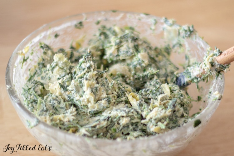 close up on mixing bowl full of spinach & artichoke filling with spatula