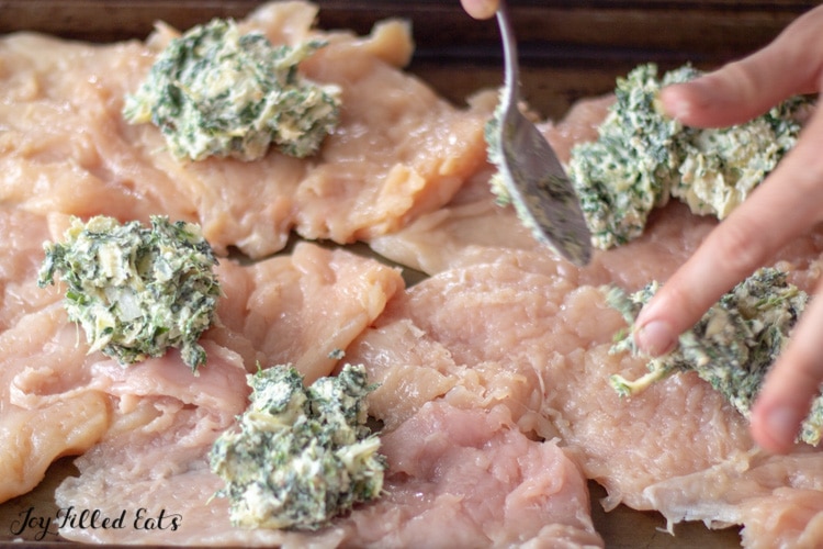 spinach & artichoke filling dolloped on pieces of butterflied chicken placed on a sheet pan