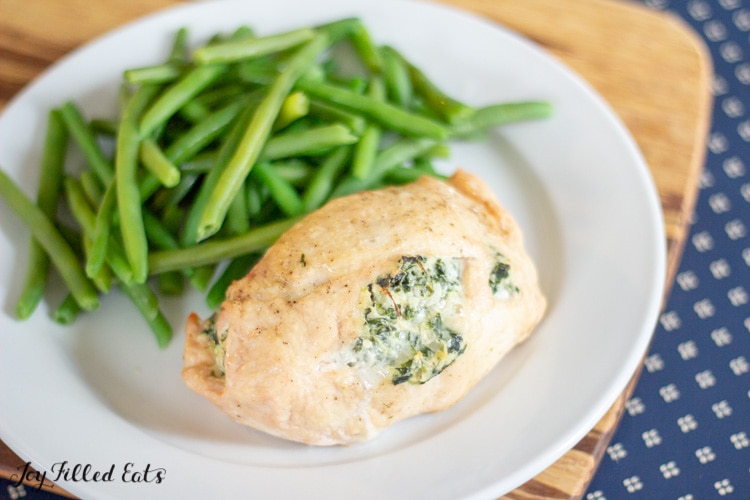 one spinach & artichoke stuffed chicken breast on a white plate served with a side of green beans