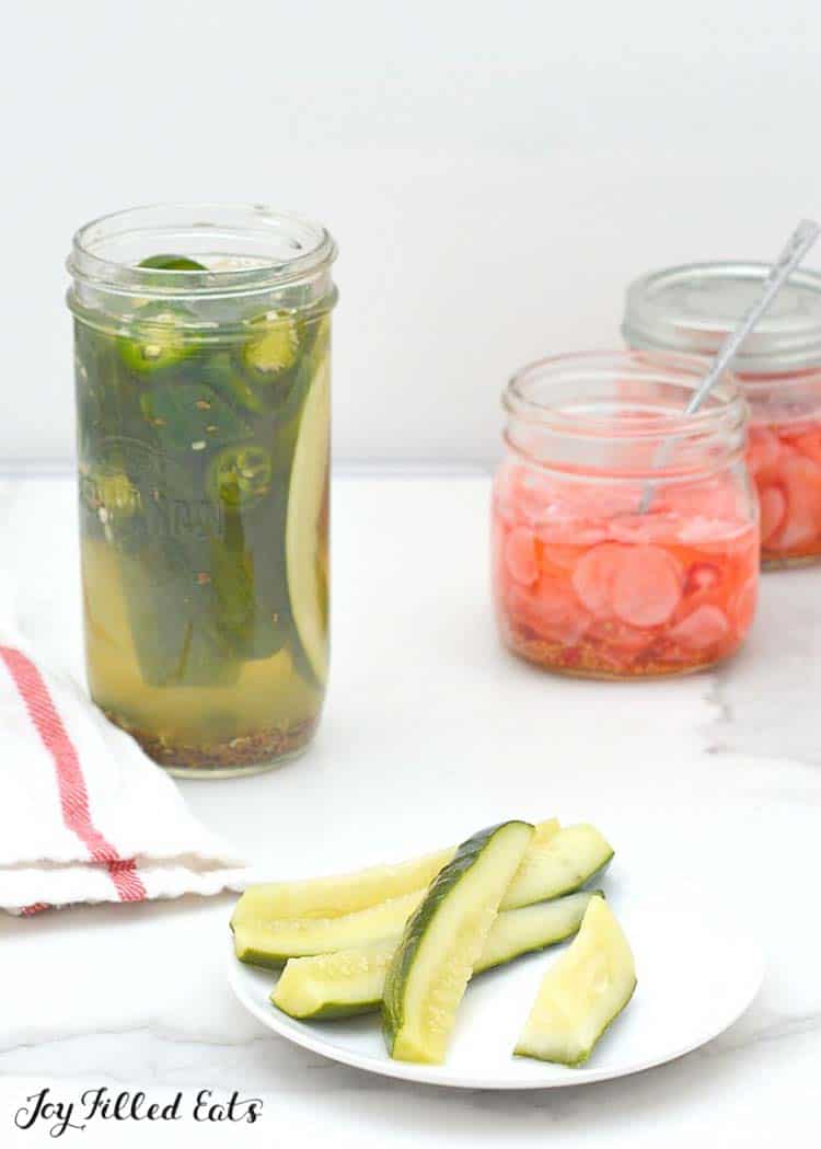 plate of pickles next to a jar of pickles and jars of radishes