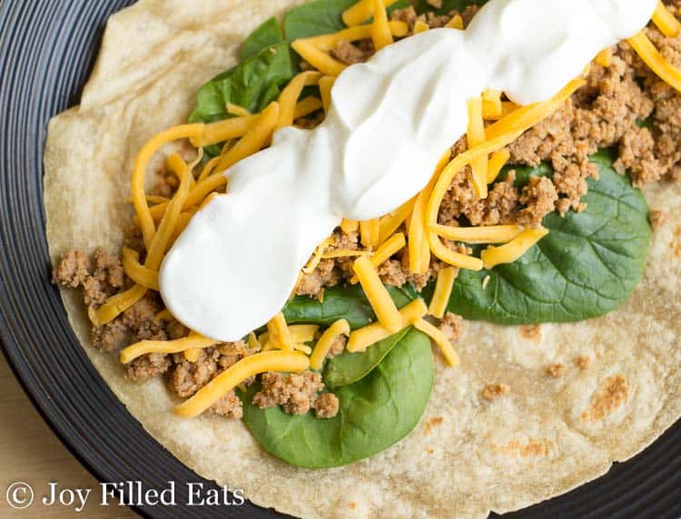 soft taco topped with baby spinach, homemade taco meat, shredded cheese and sour cream up close