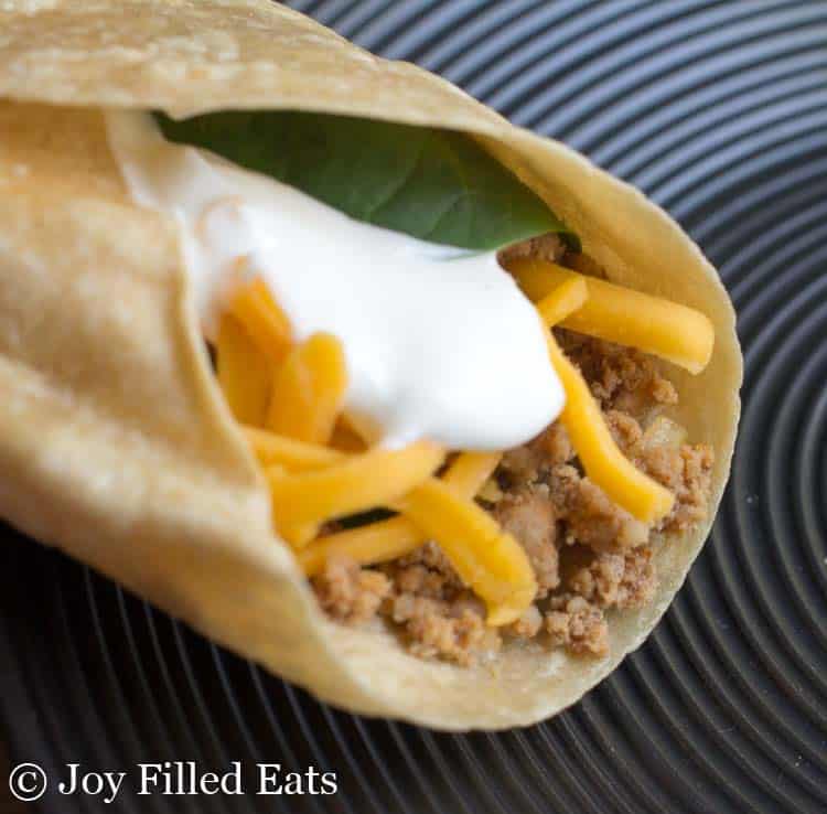 close up of rolled soft taco with baby spinach, homemade taco meat, shredded cheese and sour cream