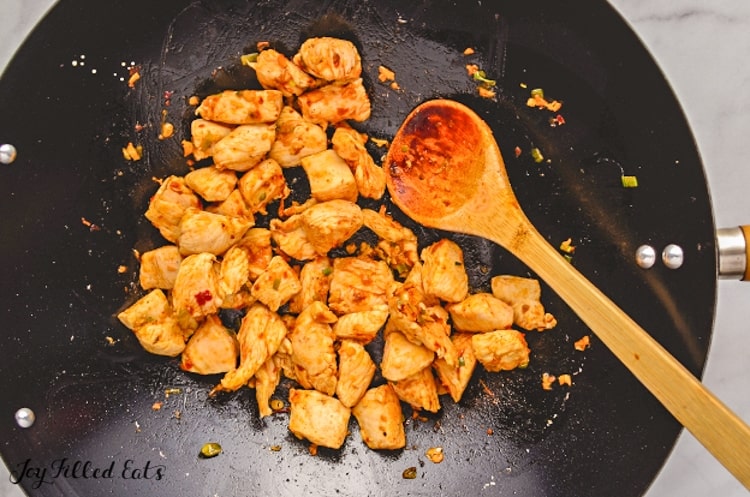 chicken pieces cooking in skillet with wooden spoon