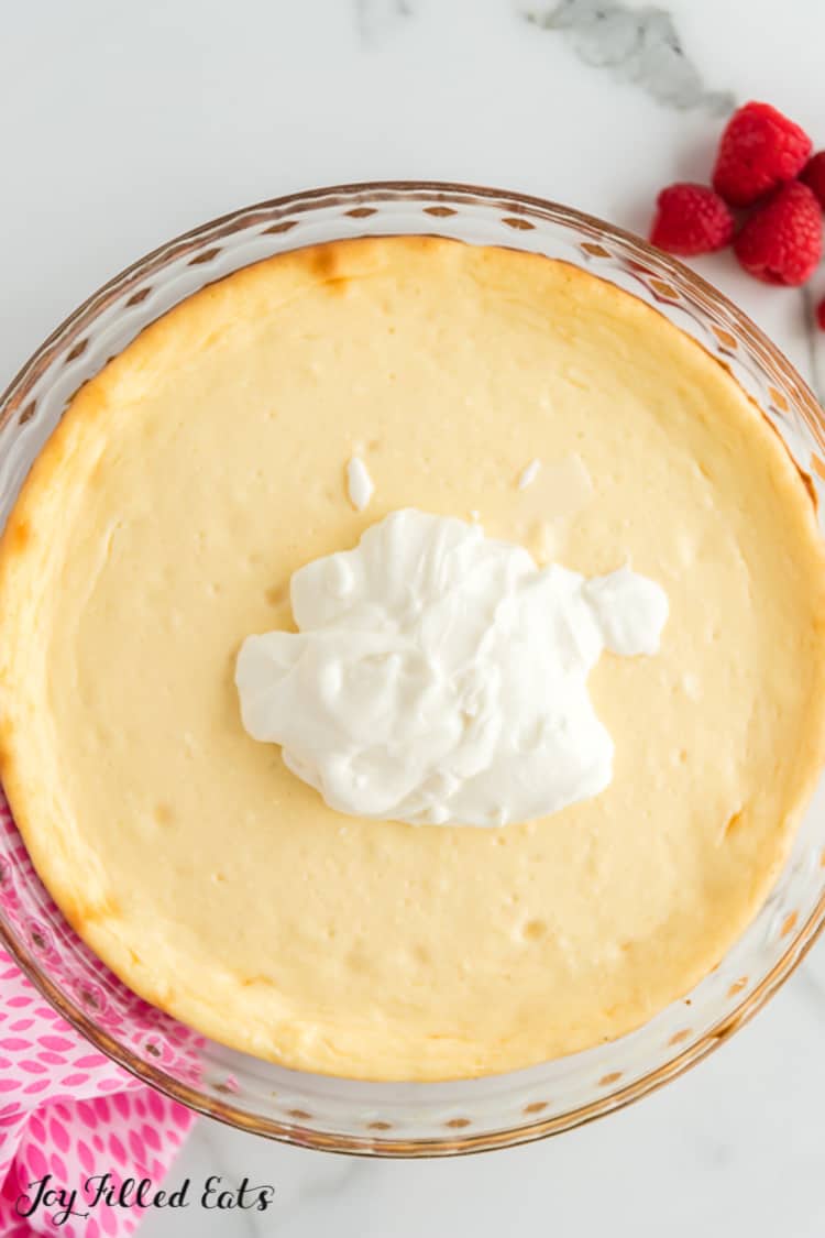 pie plate of lemon cheesecake with sour cream topping dolloped on top before being spread