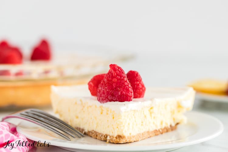 slice of keto lemon cheesecake topped with raspberries and a sour cream topping on a plate with fork