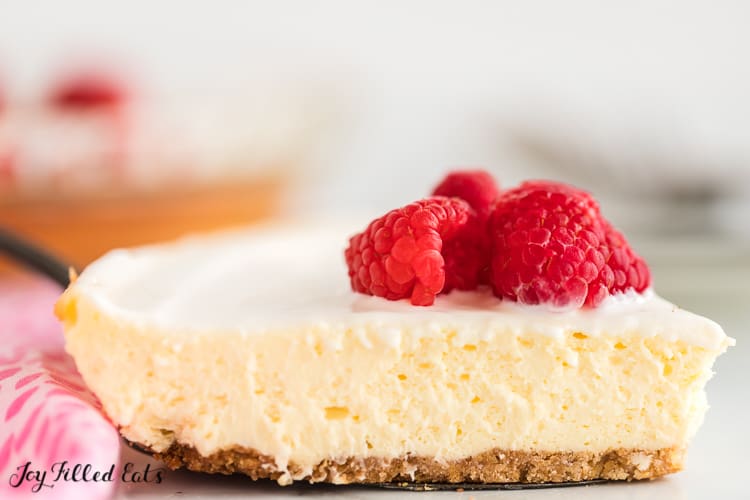 slice of keto lemon cheesecake topped with raspberries and a sour cream topping close up